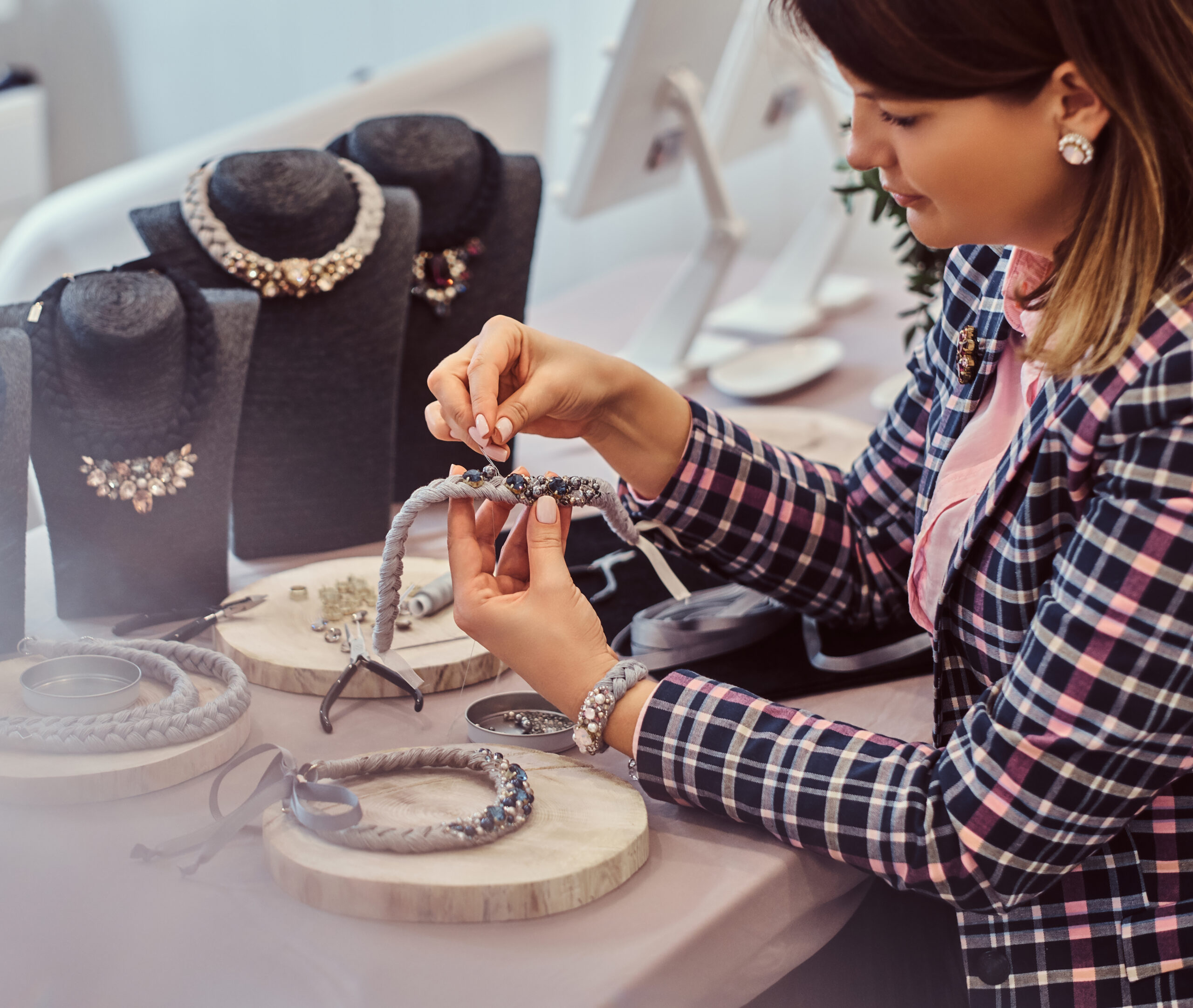Elegantly dressed woman makes handmade necklaces in jewelry workshop.